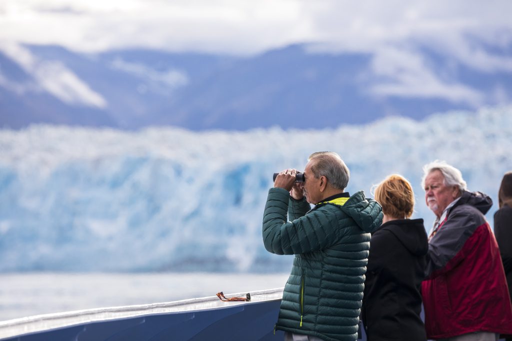 man using binoculars to look out at iceberg at sea