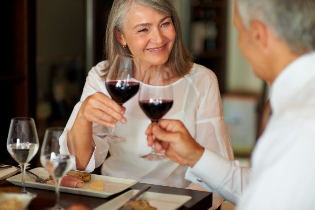 Elderly woman toasting wine with her husband wearing smart clothes for fine dining on cruise - Viking Travel