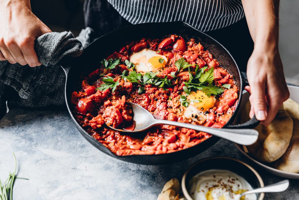 Woman preparing shakshuka with poached egg in kitchen - Viking Travel